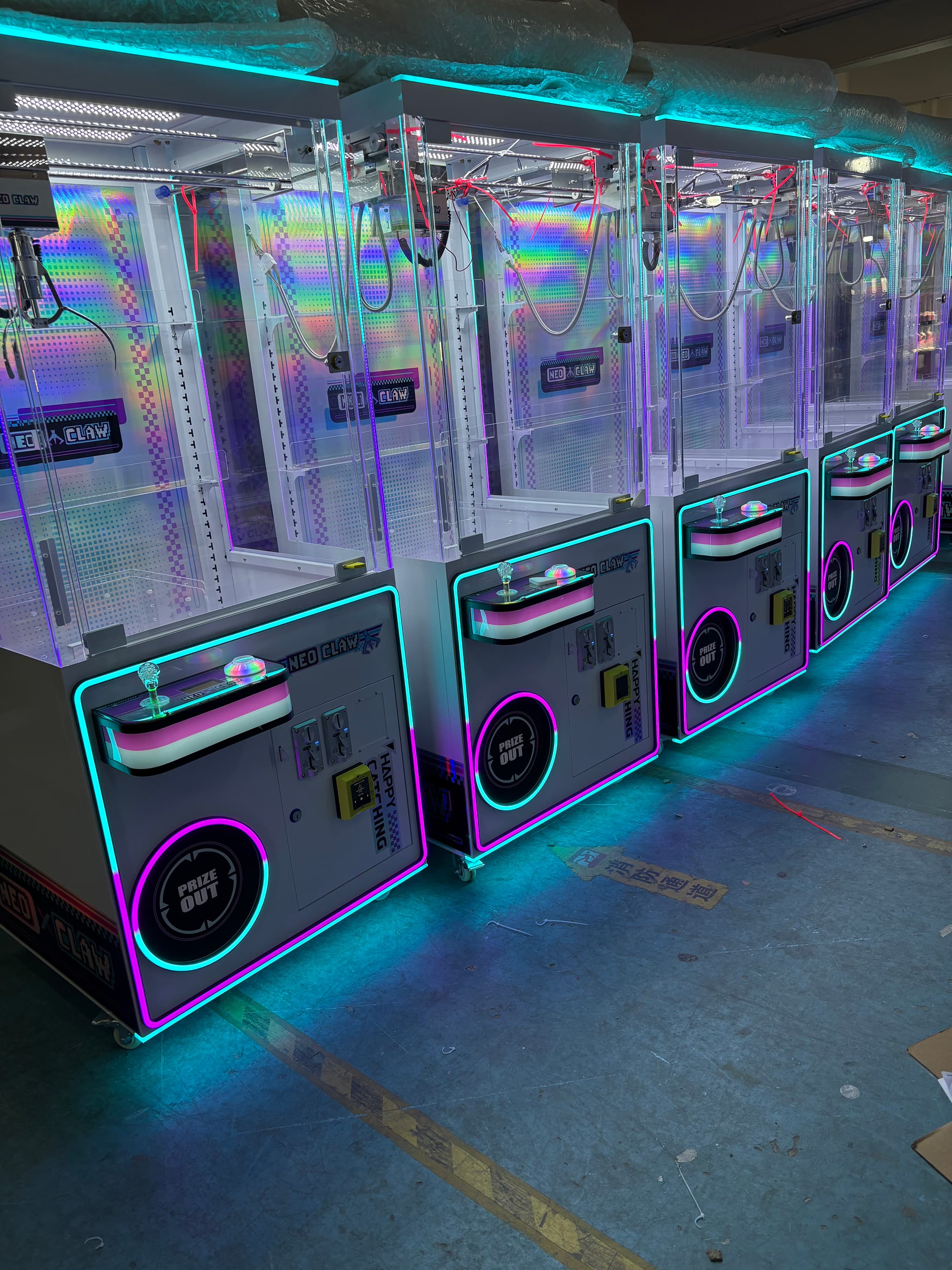 Row of white Neo Claw machines with vibrant neon LED lighting and iridescent holographic interiors.