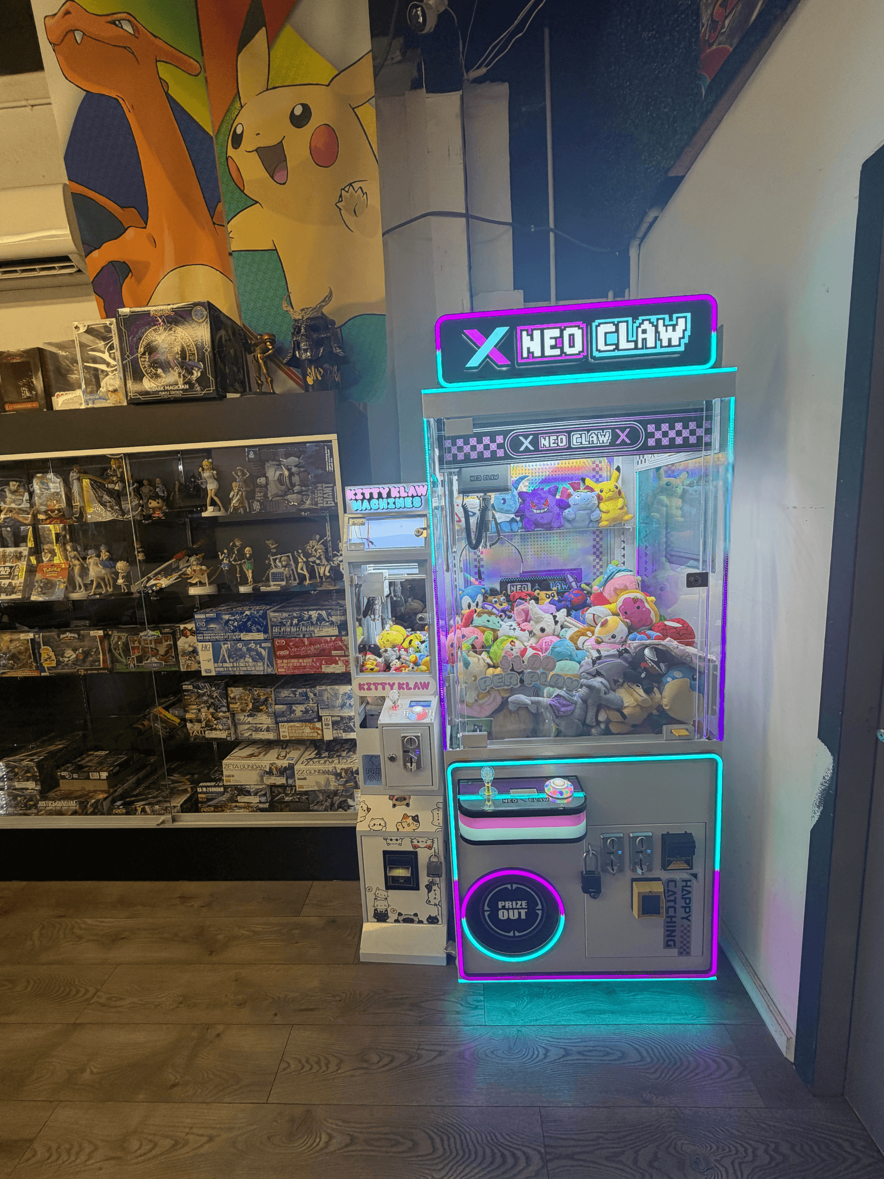 Neon-lit claw machine filled with plushies stands next to shelves of anime figurines and posters.